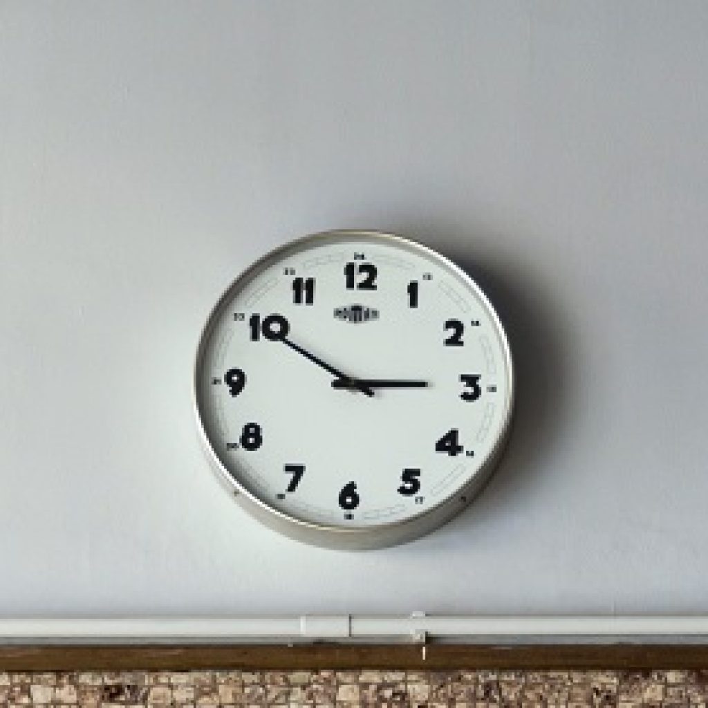 A metal round clock hung up on a white wall