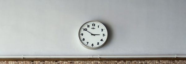 A metal round clock hung up on a white wall