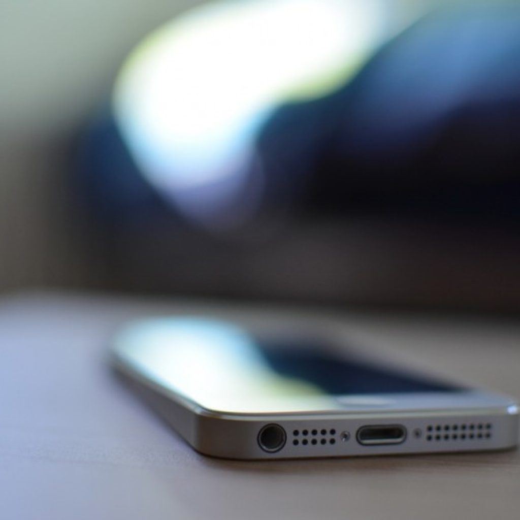 A mobile phone displaying it's speakers and charging port while laying on a table