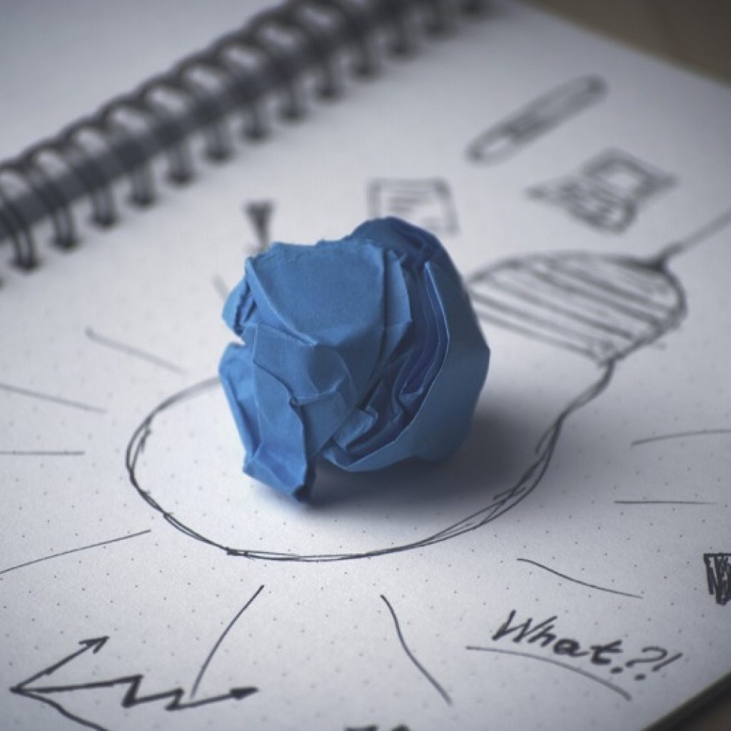 A scrunched up piece of blue paper on a notebook with a drawn light bulb on it