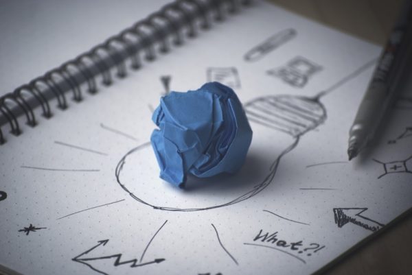 A scrunched up piece of blue paper on a notebook with a drawn light bulb on it