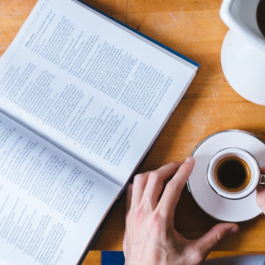 A person holding a teacup while reading at a table