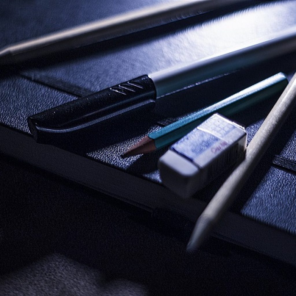 A pen, pencils and rubber on top of a black leather-bound notebook