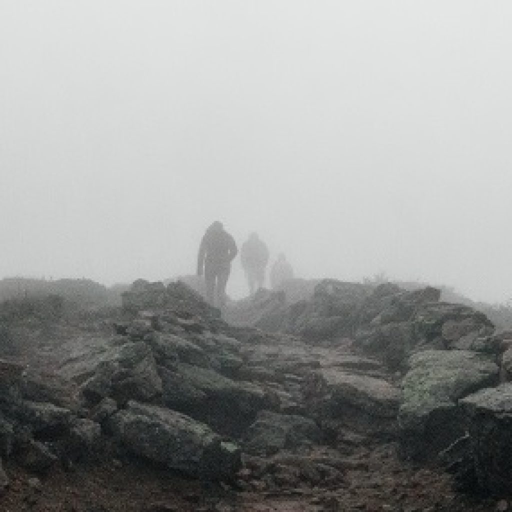 A group of three people climbing a misty rock covered hill