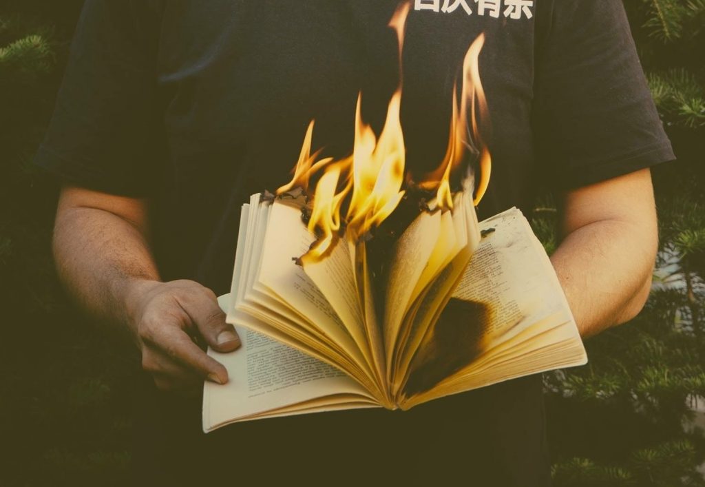 A person in a black tshirt holding a burning book