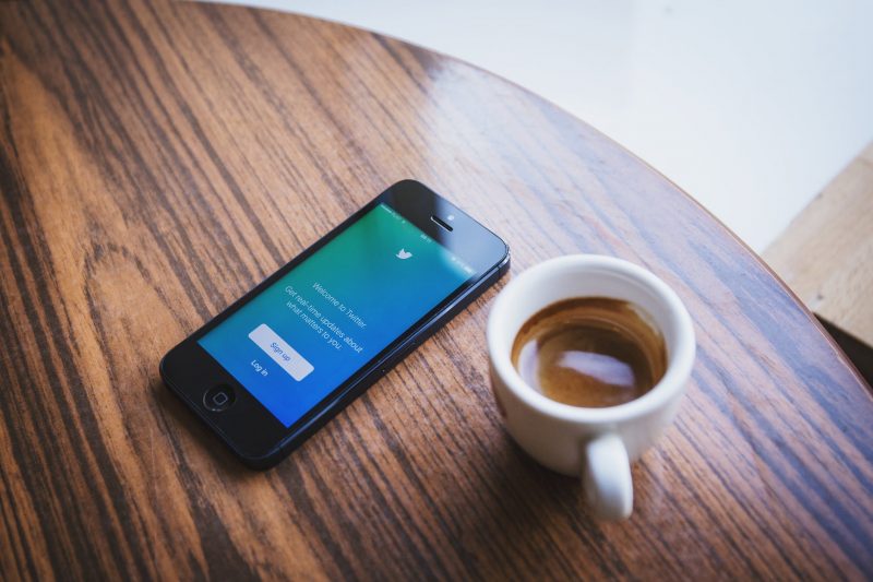 A mobile phone displaying Twitter sign in page next to a cup of coffee