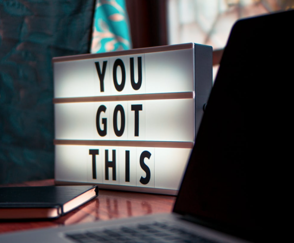 The words "You Got This" displayed on a lightup box on a desk next to a laptop and notebook