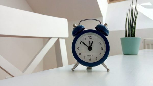 Navy alarm clock standing on a white desk infront of a plant