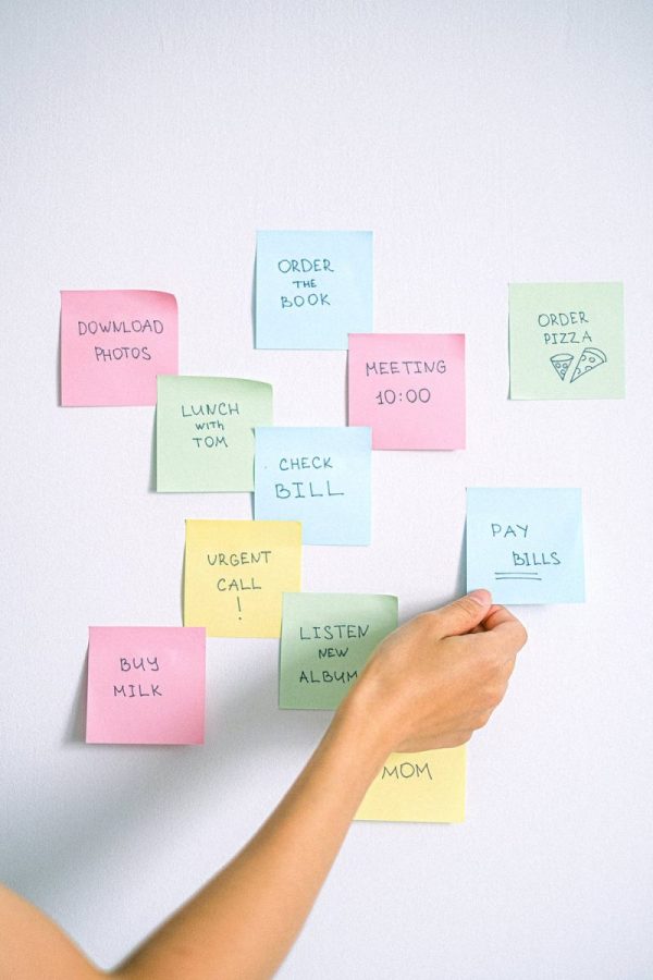 A hand placing some colourful post it notes on a white wall which display different tasks