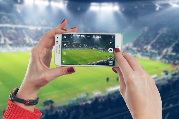 A woman filming a football stadium through her SAMSUNG mobile phone