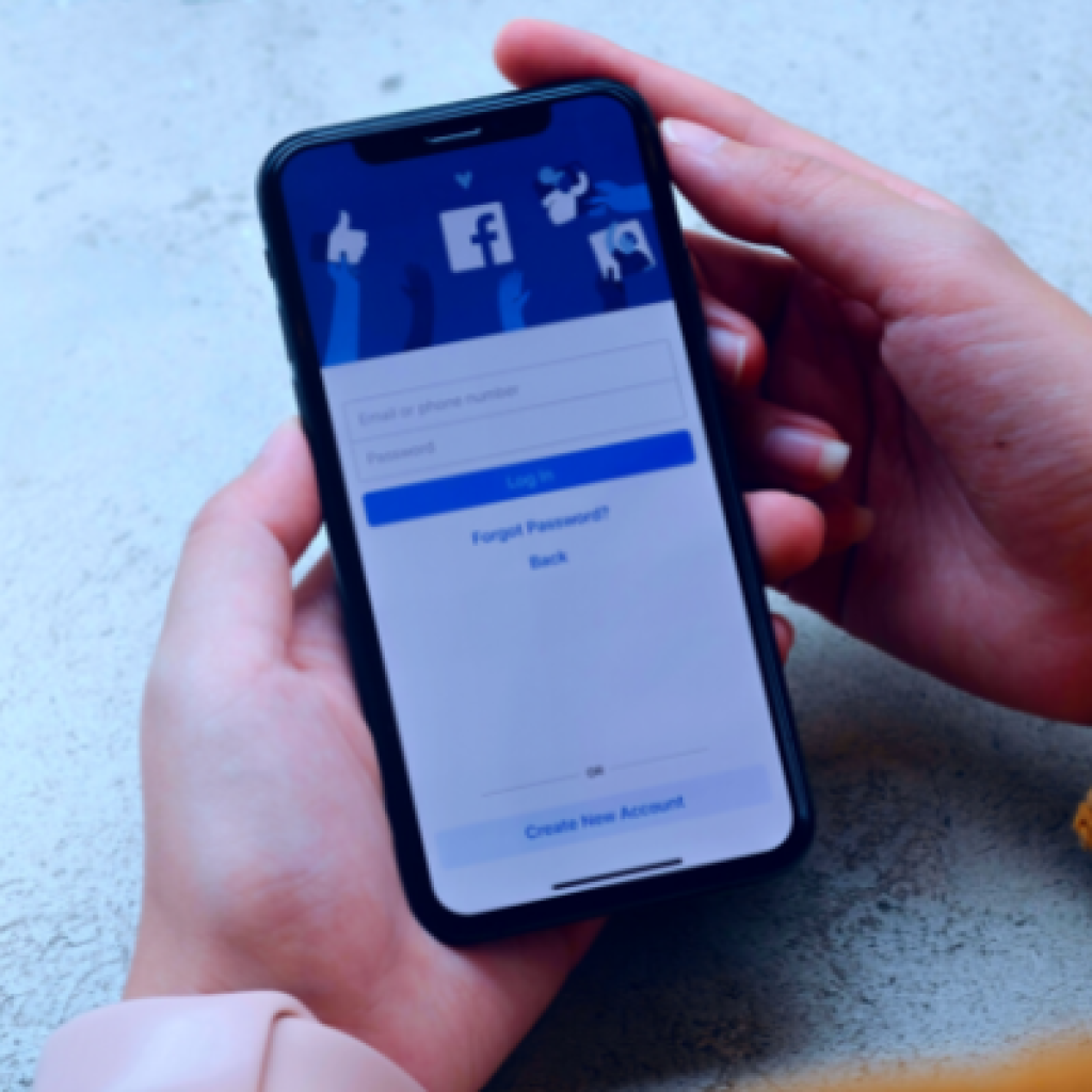 Hands holding a mobile phone displaying the Facebook app log in screen