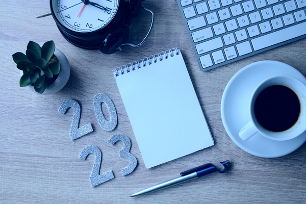 A notepad, pen and alarm clock on a desk next to the numbers 2023