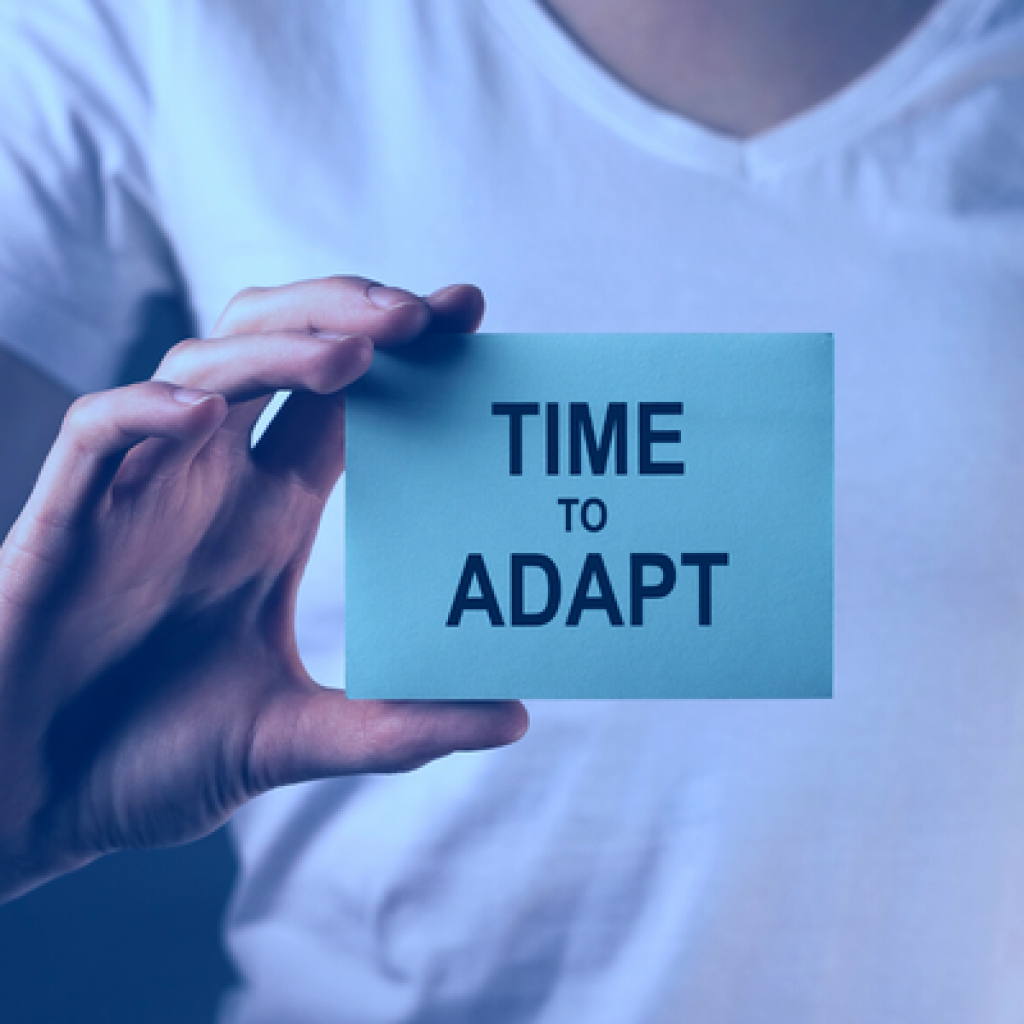 A person in a white t-shirt holding up a blue card with the words "Time to Adapt" written on the front