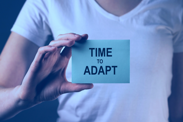 A person in a white t-shirt holding up a blue card with the words "Time to Adapt" written on the front