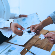 Two people holding pieces of a jigsaw together on top of business documents