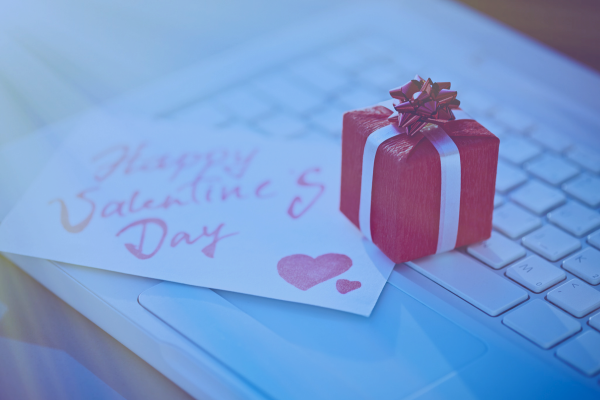 A small red gift box with a ribbon and a handwritten "Happy Valentine's Day" card on a laptop keyboard